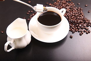 black liquid in white ceramic teacup beside coffee beans