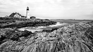 grayscale photo of lighthouse on rocky cliff