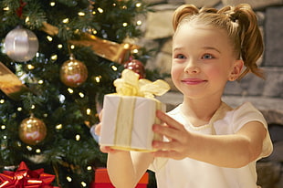 smiling girl holding Christmas gift in front of tree