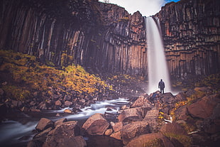 person standing in front of water falls during daytime HD wallpaper