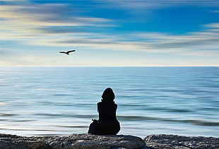 silhouette of person sitting on rock near sea