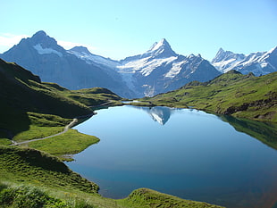 body of water surrounded by grass with snow mountain background