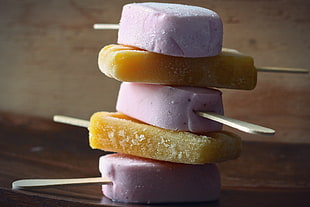 three pink and two yellow ice Popsicles stacked in closeup photography