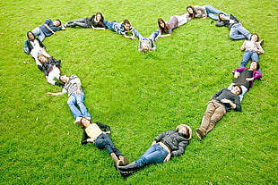group of people lying on green grass forming heart