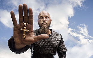 man in chainmail holding gold-colored cross pendant