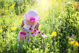 girl in pink hat and white tank dress picking pink flowers