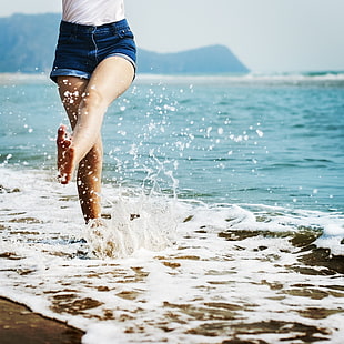 girl in blue short shorts running on seashore