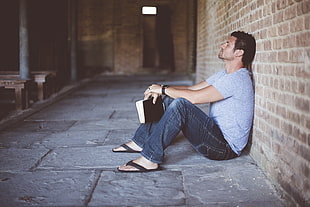 man in gray crew-neck shirt sitting while holding black bible