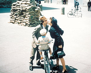 couple kiss beside child on a bike