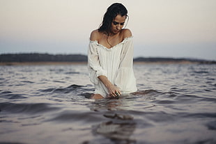woman in white long sleeve off-shoulder shirt standing on body of water during daytime