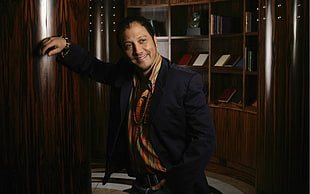 man in black suit jacket standing near brown wooden shelf