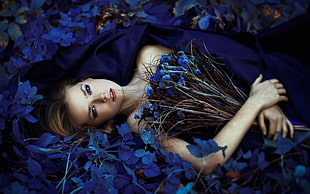 woman wearing blue dress holding bouquet of blue flowers while laying on blue bed of flowers