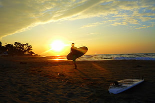 person holding surfboard during sunset
