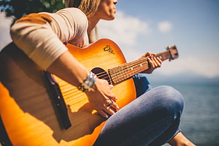 woman playing dreadnought acoustic guitar beside body of water during day time