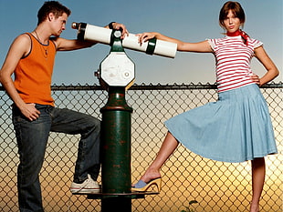 man wearing orange tank top holding telescope beside girl wearing striped shirt and blue skirt