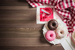 three doughnut in white ceramic saucer beside drinking glass