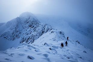 three people climbing snow covering mountain