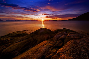 landscape photography of rock formation near body of water during sunset