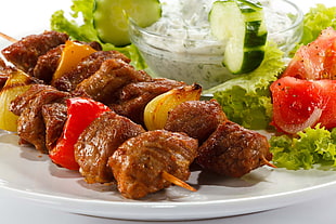 kebab with vegetable salad and white dip on white ceramic plate