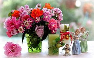 selective focus photography of bouquet of assorted flowers beside pillar candles and angel figurines