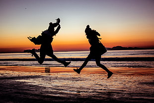 silhouette of two woman jumping near sea during susnet