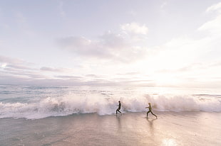 two person running on seashore