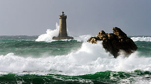 photo of brown lighthouse with waves splashing