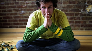 man in green long-sleeved shirt sitting on brown wooden flooring