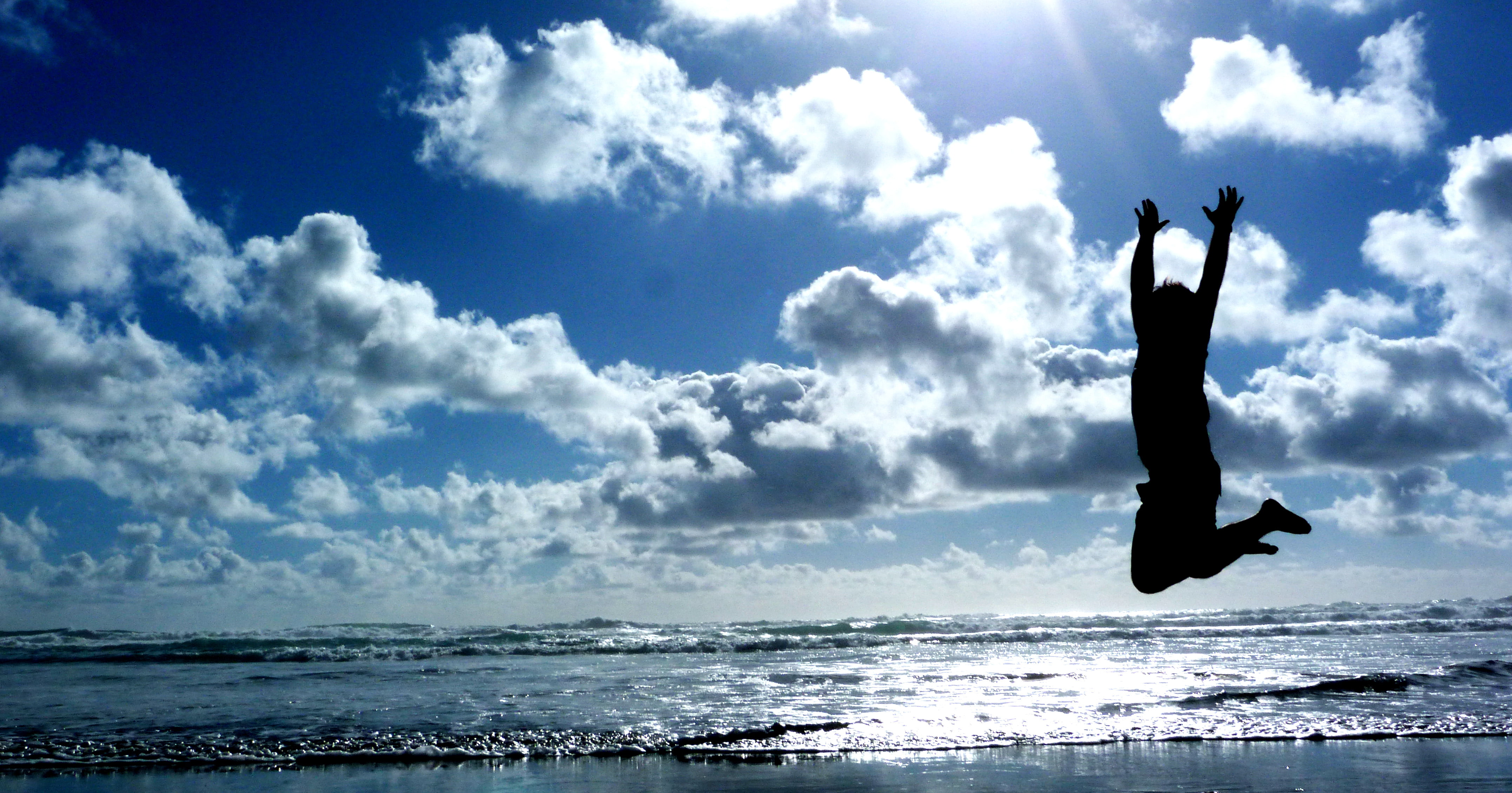 silhouette photography of  person jumping near beach shore during daytime