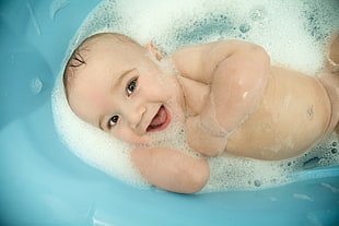 photography of baby playing with bubbles on blue tub