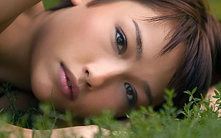 black haired woman lying head on green grass field
