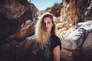 blonde woman wearing black top standing near brown rock