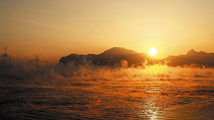 body of water with evaporating smokes during golden hour