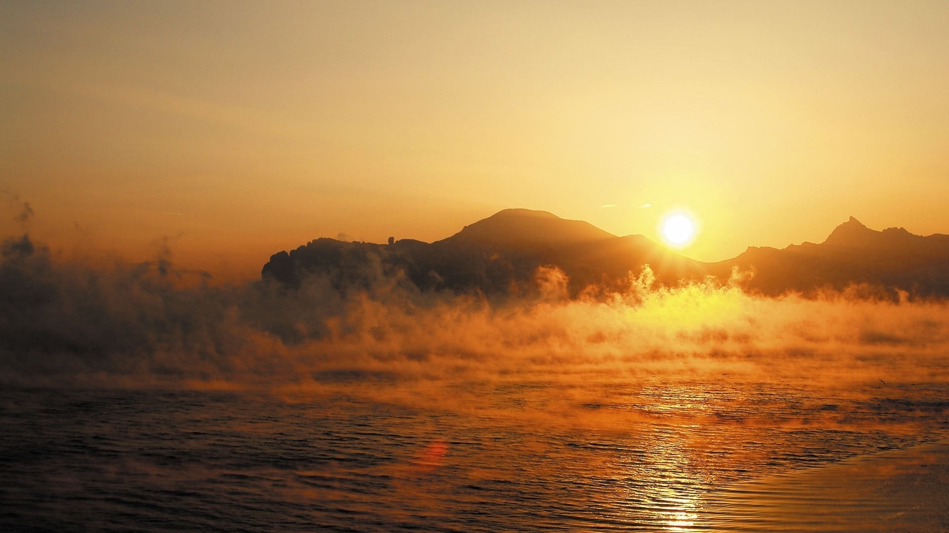body of water with evaporating smokes during golden hour