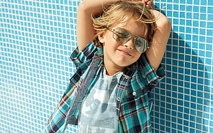 boy in plaid shirt leaning beside wall