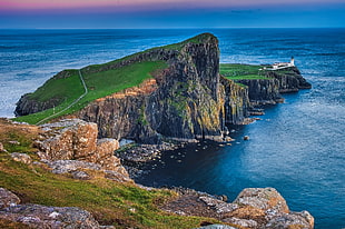 white lighthouse on green grass field and large rock formation near body of water, neist point