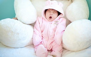 baby in white zip-up hooded pram suit with big white animal plush toy behind