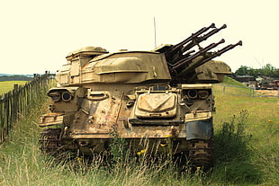 brown combat tank on field with green grasses and wooden fence