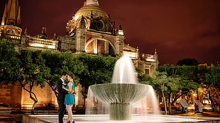 photo of man and woman beside fountain during nightime