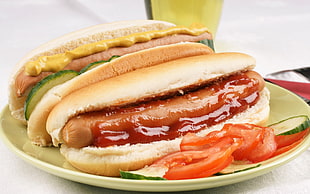 hotdog on buns with ketchup and sliced tomatoes on top of round yellow ceramic plate