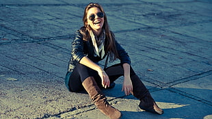 woman wearing black jacket, pants, and brown boots sitting on concrete ground