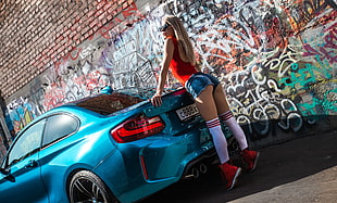 woman wearing blue short shorts leaning on blue coupe