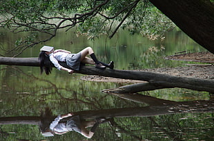 woman wearing white dress shirt and gray skirt laying on wooden branch