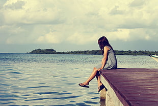 woman sitting on brown wooden bridge dock during daytime