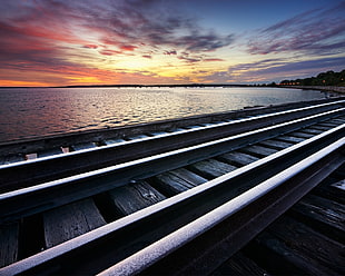 photo of railroad near body of water during golden hour HD wallpaper