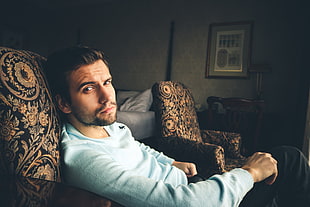 man wearing teal long-sleeved shirt sitting on black and brown floral sofa