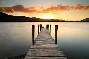 brown wooden boardwalk near body of water during sunset