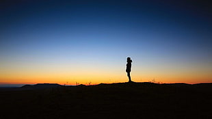 silhouette of a person wearing a hoodie standing on land against a golden hour light