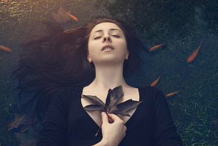 woman in black v-neck long-sleeved top holding black maple leaf while floating on water with orange school of fish