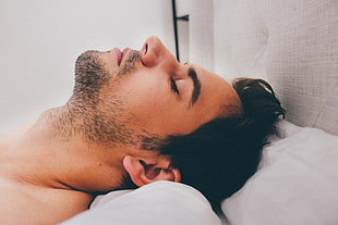 man lying on bed with white pillow inside the room